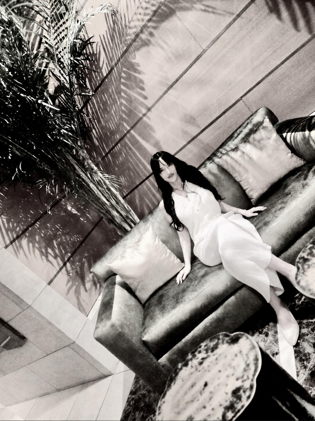 Cis-gender woman therapist sits on a sofa, wearing a white dress, with long black hair